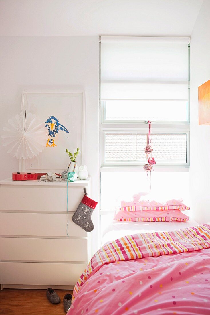 Bed with pink bed linen below window and Christmas stocking hung on white chest of drawers in girl's bedroom