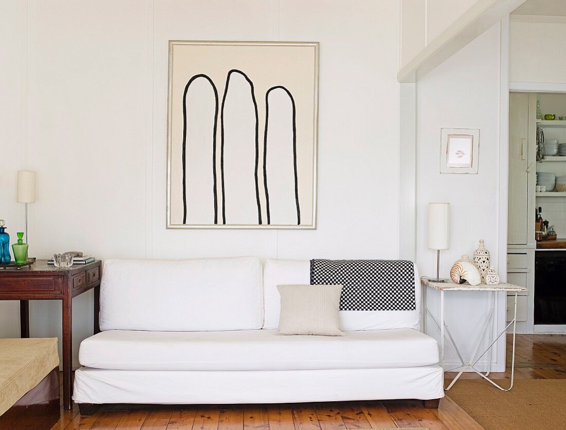 weiße minimalistische Couch vor Wand mit gerahmtem Bild, seitlich breiter Durchgang