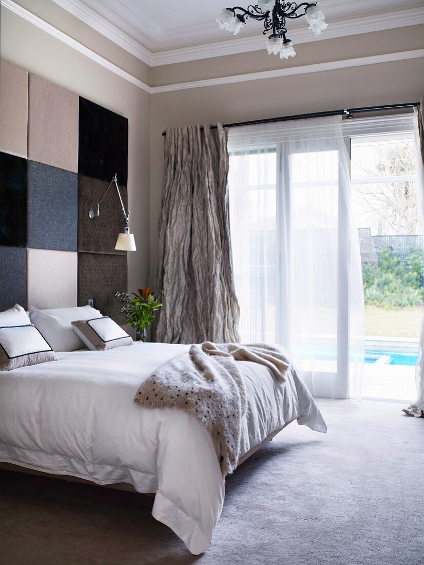 Double bed against wall with panels in various shades in traditional interior; open terrace door with view of pool