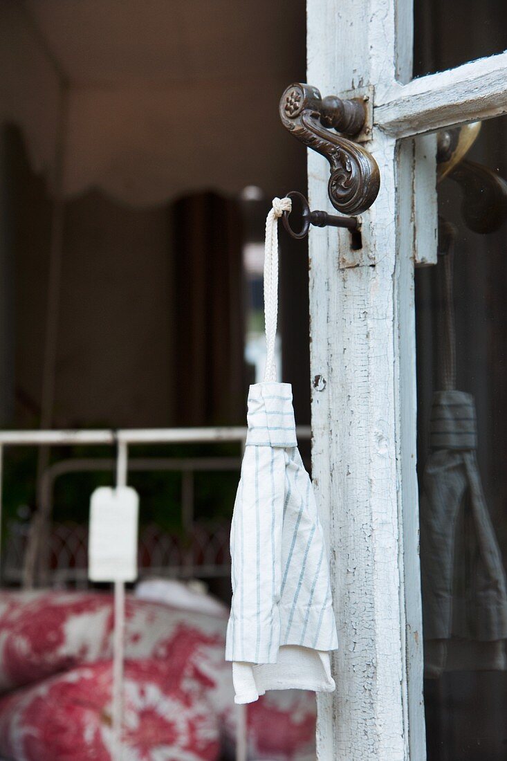 Schlüssel mit Stoffanhänger an der alten Fenstertür eines französischen Landhauses; im Hintergrund Preisschild an Metallbett