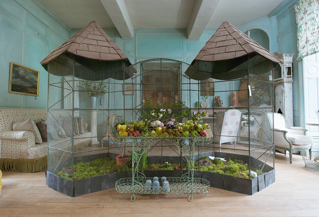 Antique bird aviaries and wire shelves with garden ornaments in front of upholstered furniture all for sale in an old French country house