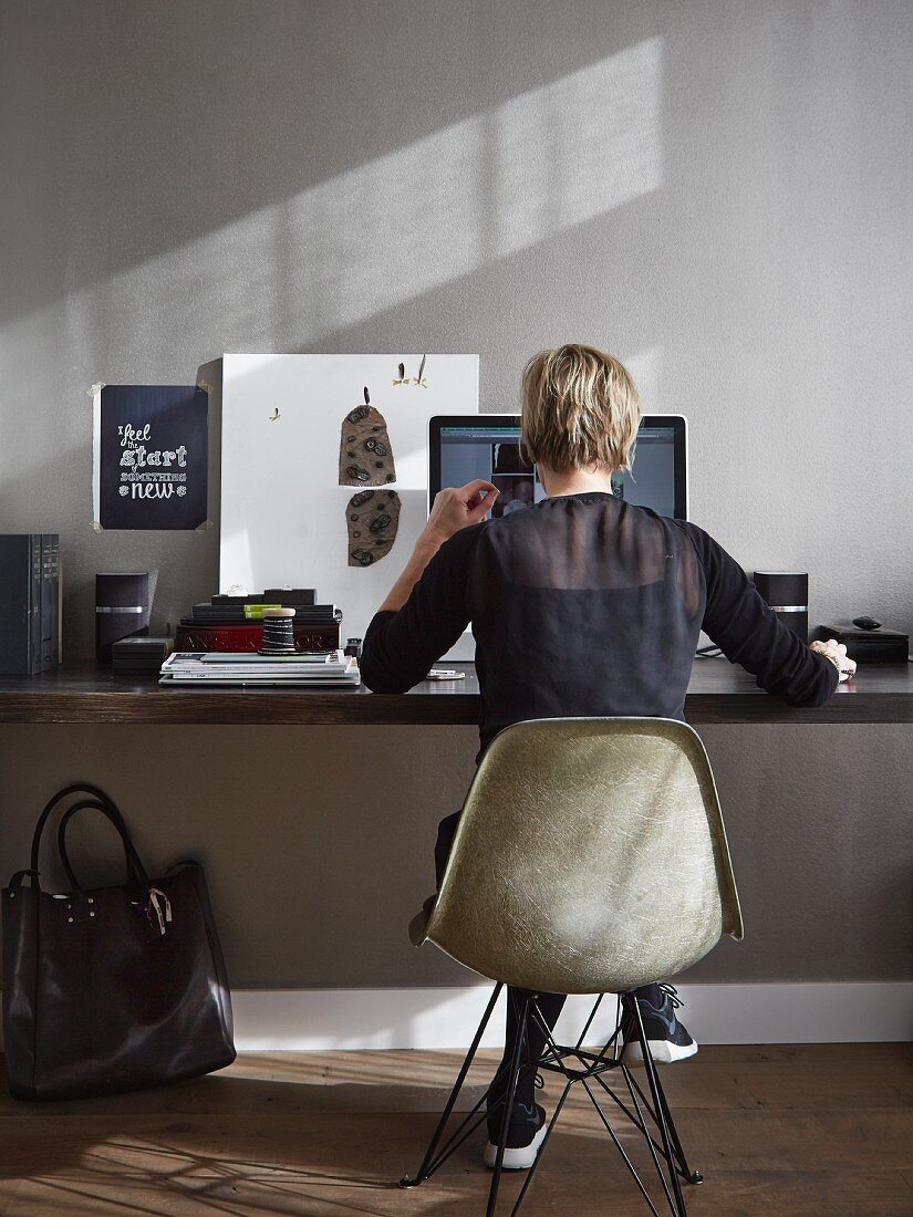 Woman sitting on Eames chair at desk in grey-painted home office