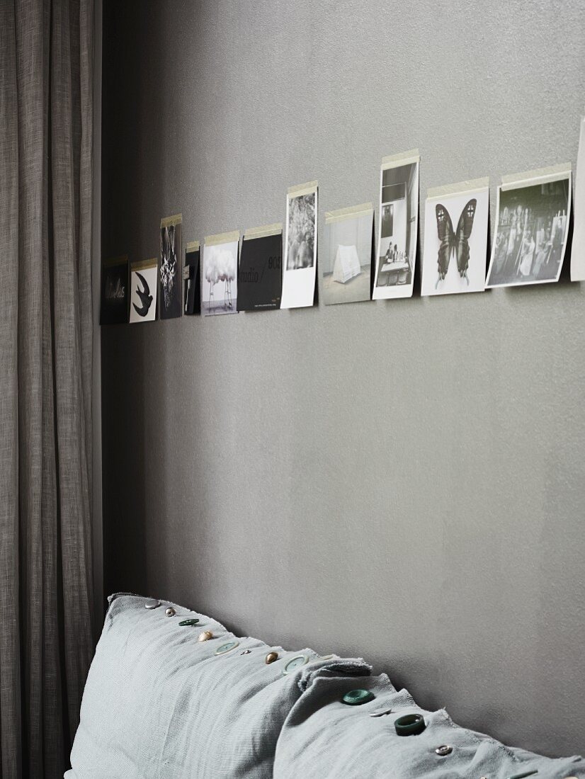 Schwarz-weiße Fotos an grau getönter Wand über Sofapolster mit verschiedenen Schmuckknöpfen