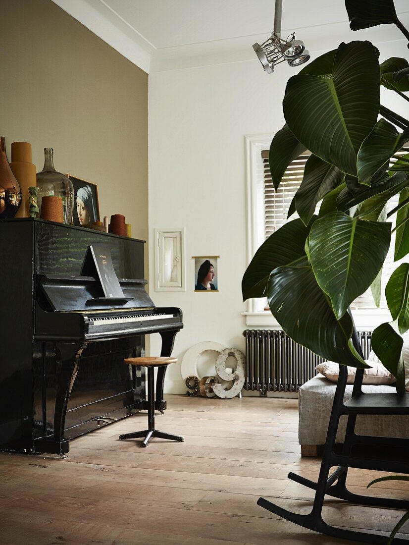 Old piano decorated with vases opposite sofa with houseplant leaves and rocking chair in foreground