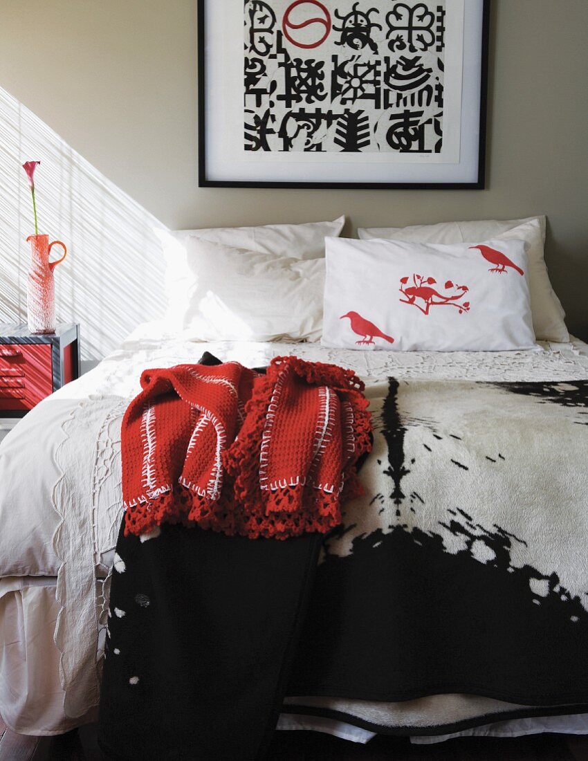 Bild mit schwarzweissen Ethno-Mustern über einem französischem Bett mit verschiedenen Strukturdecken und Vogelprint auf Kissen; seitlich einfallendes Sonnenlicht