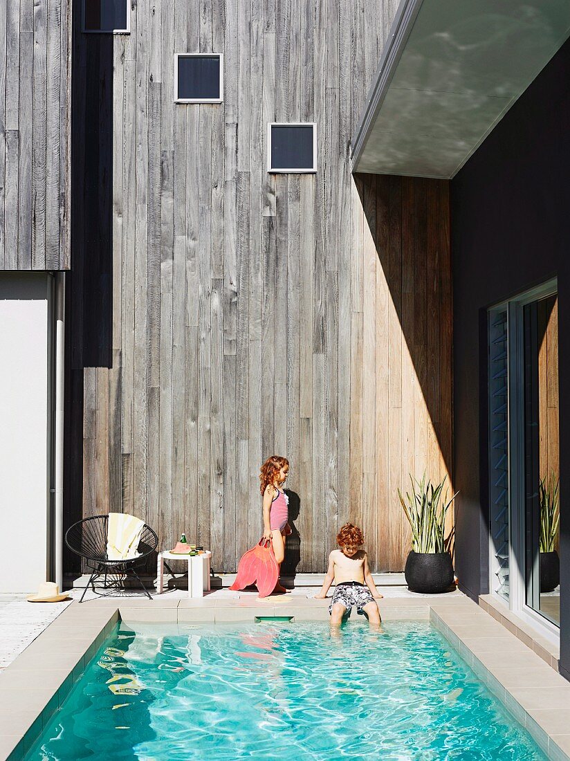 Children next to pool of Australian beach house against wooden facade weathered to a silvery grey