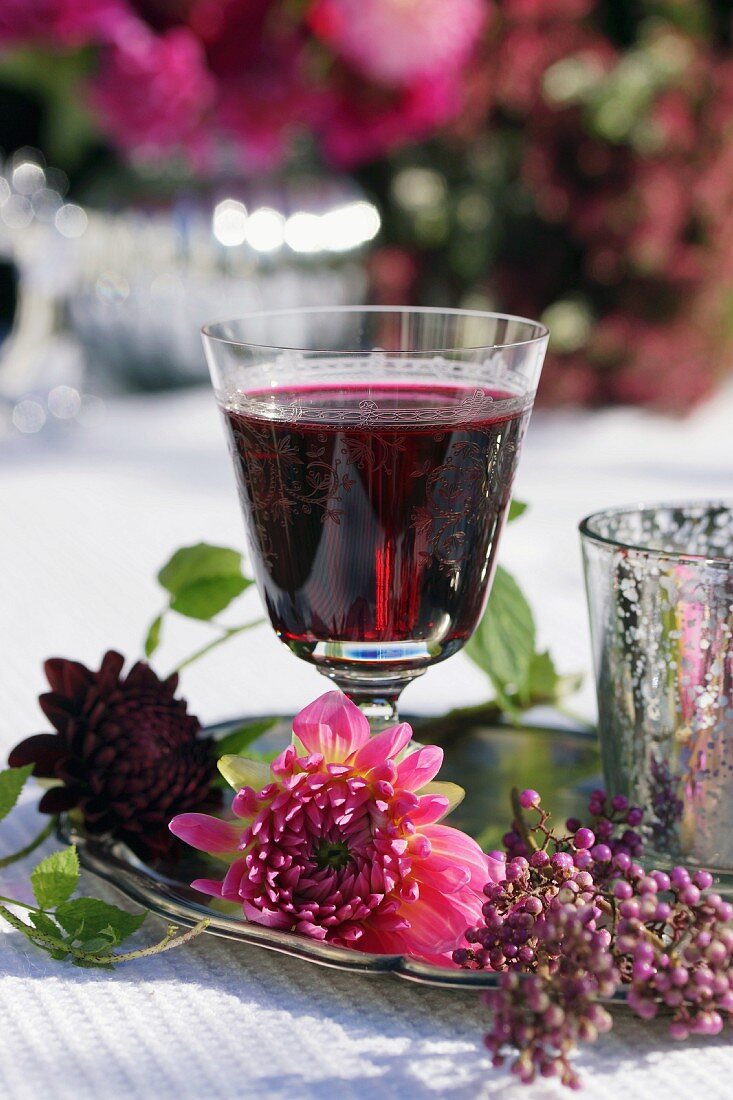 Dahlienblüte vor Rotweinglas und Callicarpa auf Silbertablett