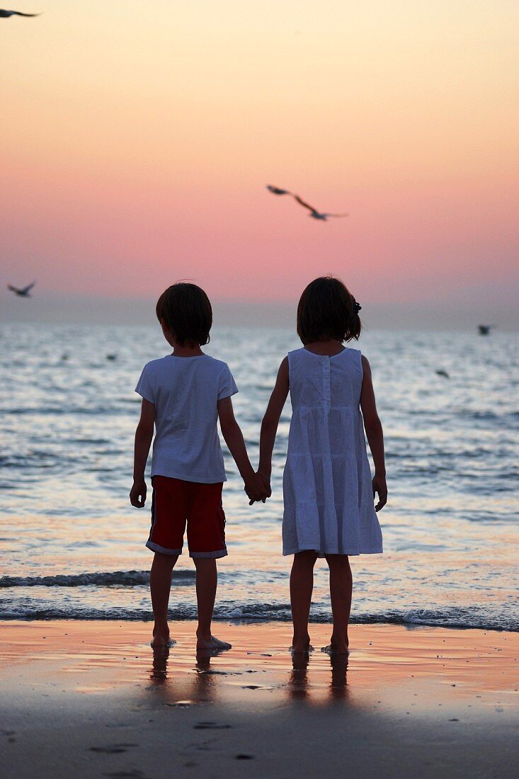 Little boy and girl hand in hand on beach at sunset
