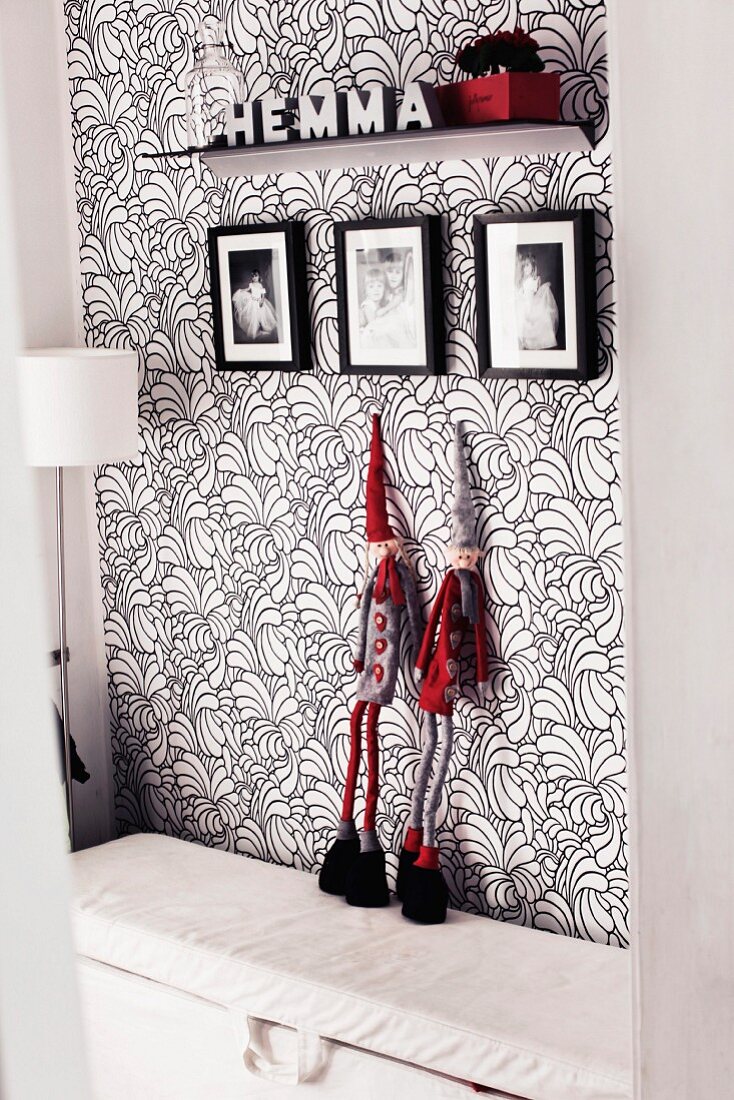 Schwarz-Weiß-Rot: An floral gemusterte Tapetenwand angelehnte Figuren mit Zwergenmützen, darüber Kinderfotos und ein Deko-Bord