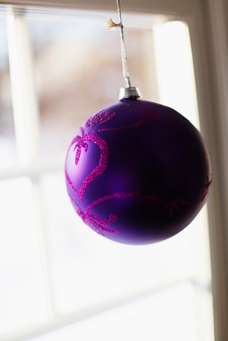 Purple Christmas bauble with glitter print hanging in window
