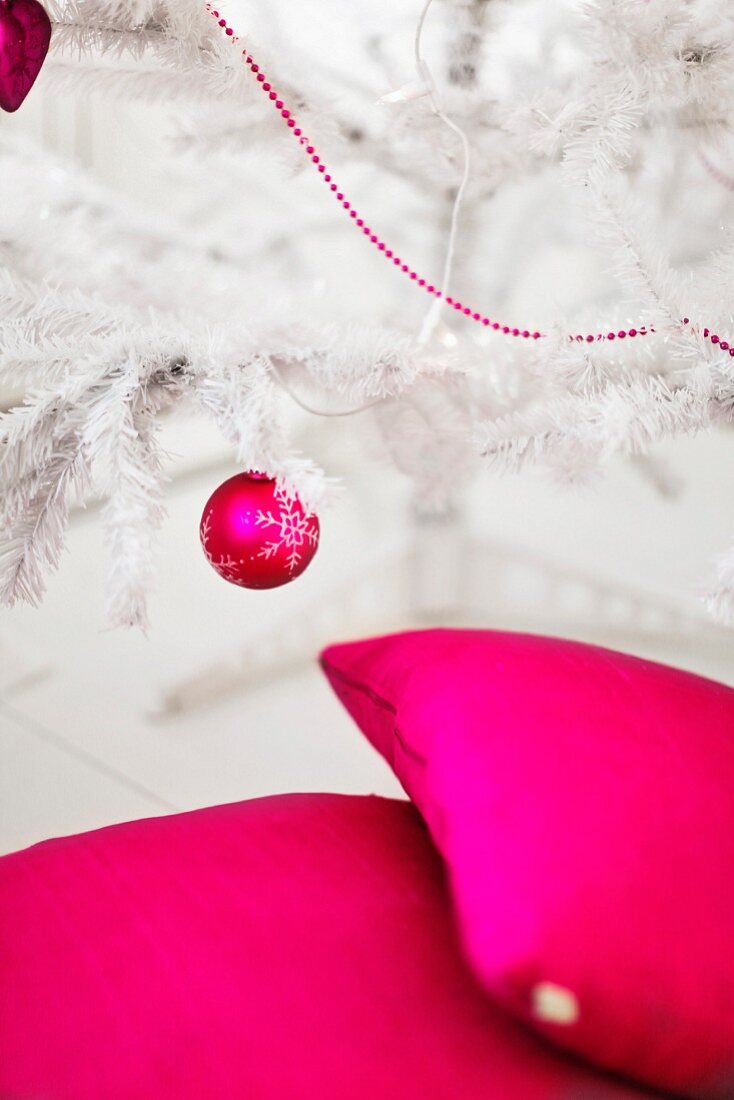 Kissen, Weihnachtskugel und Zierkette in leuchtendem Magenta an weißem, künstlichem Christbaum