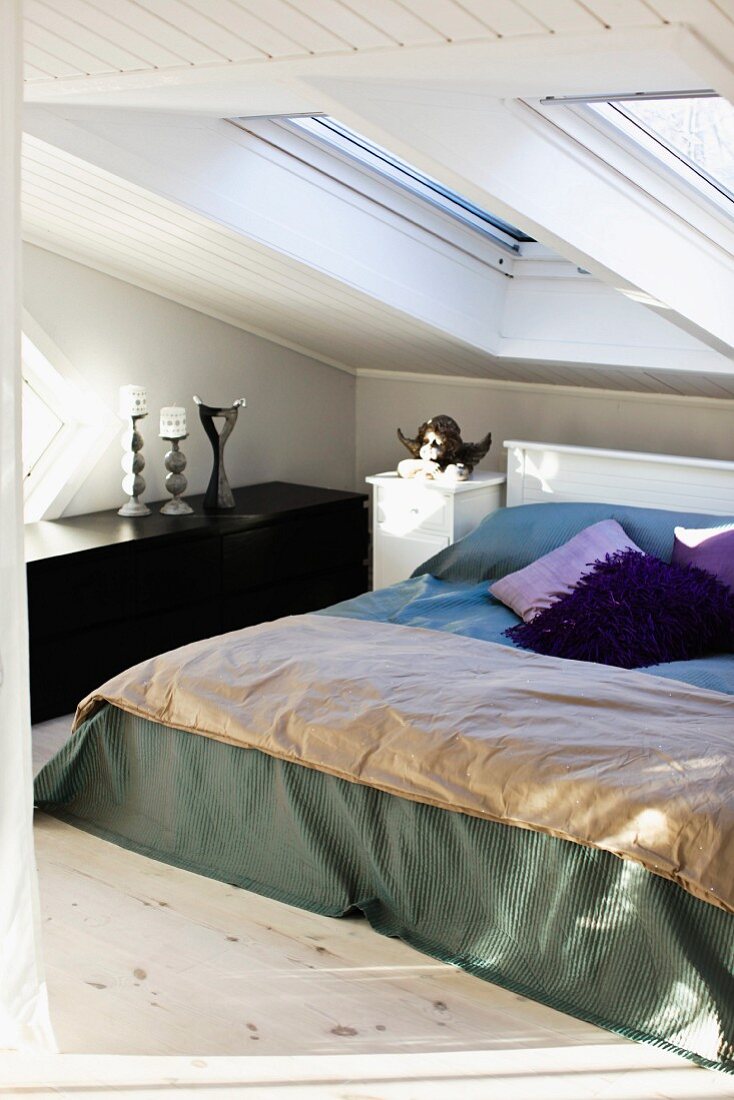 Double bed with blanket and scatter cushions below skylights in vintage attic bedroom