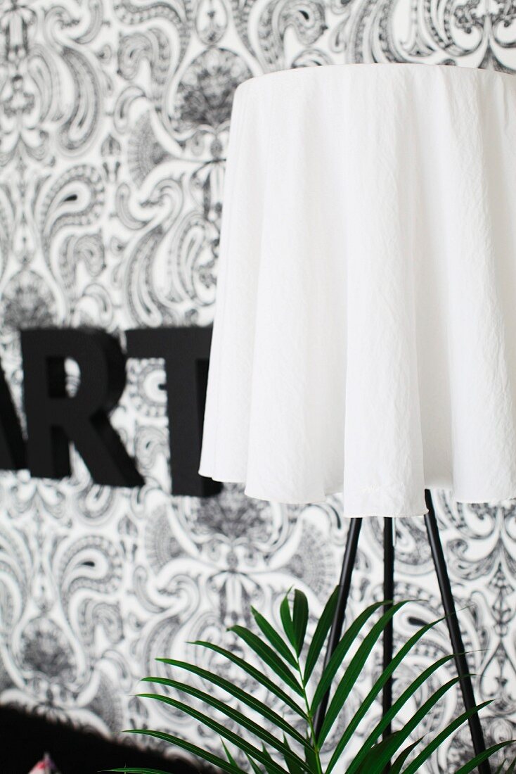 Stehleuchte mit weißem Lampenschirm vor schwarz-weiß tapezierter Wand