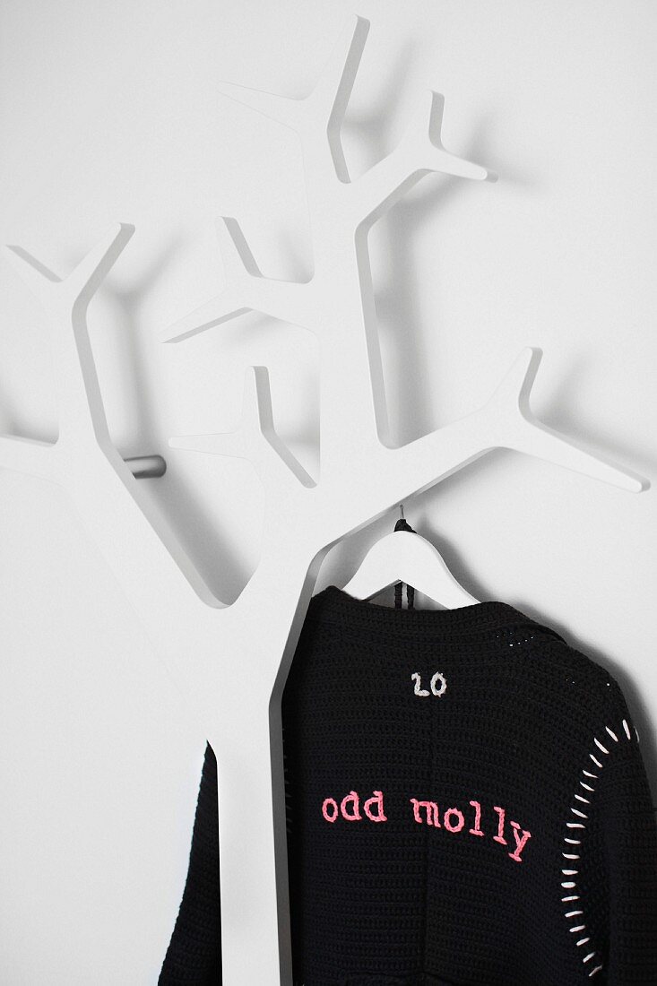Black cardigan hanging on coat rack in shape of stylised tree made from white-painted wood