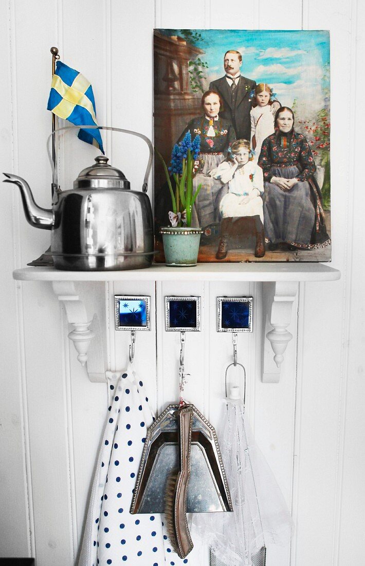 Vintage kettle next to painted family portrait on bracket on white wooden wall