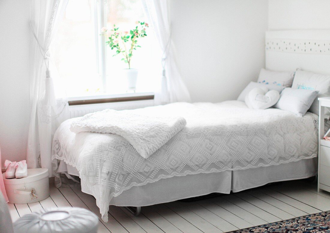 White, lacy bedspread on bed below window in rustic interior