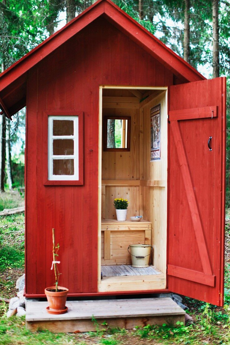 Blick durch die geöffnete Tür eines schwedischen Toilettenhäuschens aus rot lasiertem Holz