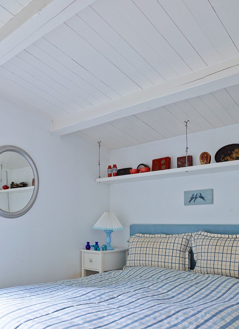 Doppelbett mit karierter Bettwäsche in rustikalem Schlafzimmer mit weiss gestrichener Holzdecke