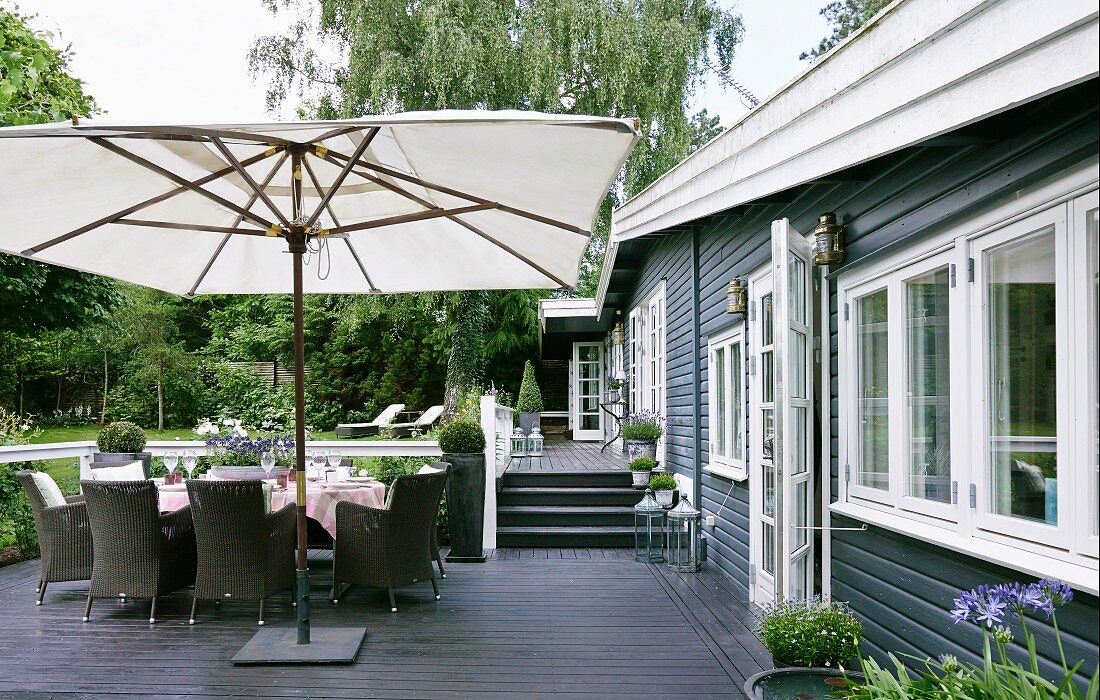 Modern outdoor furniture and white parasol on terrace; terrace floor and house facade in dark wood panelling