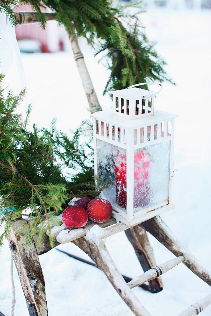 Lantern, apples and fir branches on rustic wooden stand in snowy garden