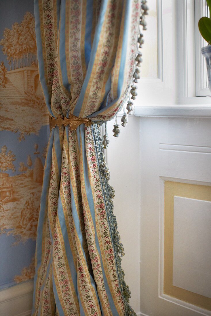 Drapierter Vorhang mit kleinen Quasten vor Fenster in traditionellem elegantem Ambiente