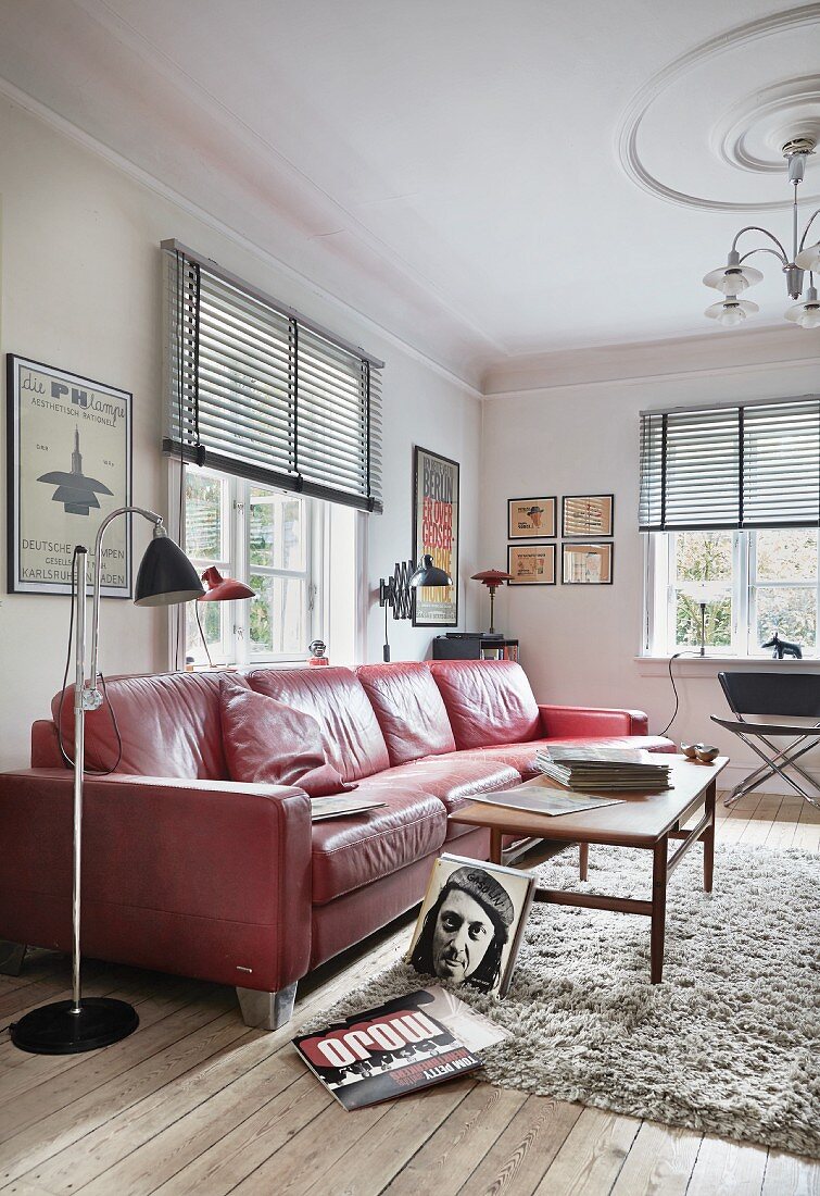 Standard lamp next to red, retro leather sofa and wooden coffee table on flokati rug in period living room with modern ambiance