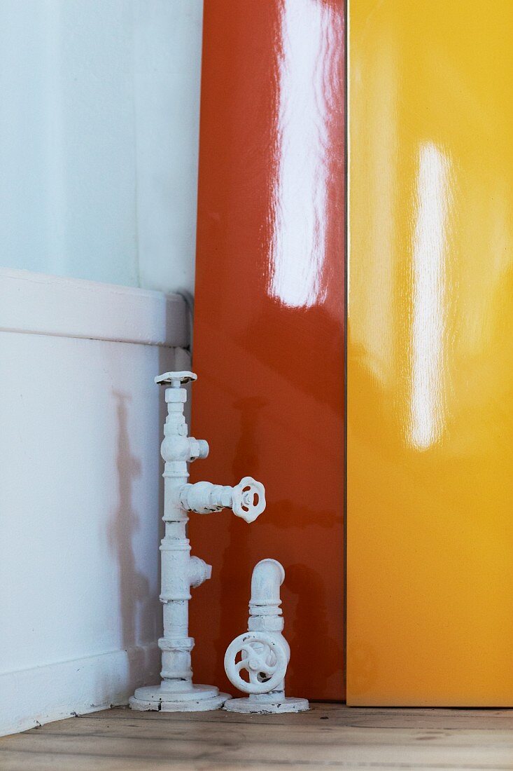 Vintage water pipes with stop cocks in front of lacquered panels in bright orange and yellow