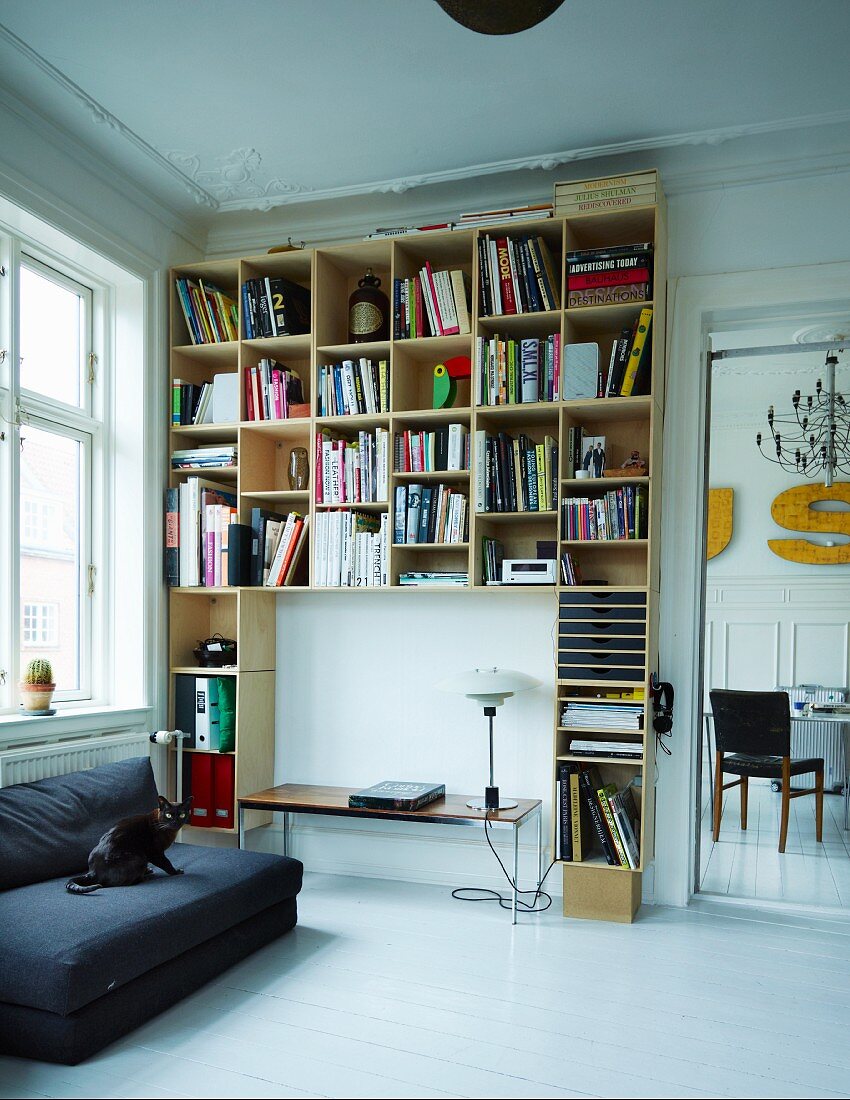 Black sofa next to shelving made from stacked wooden modules against wall in period apartment