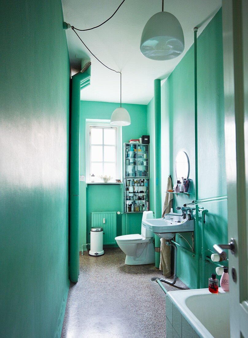 Blick durch offene Tür in mintgrün getöntes, schmales Altbau-Bad mit weißen Hängeleuchten