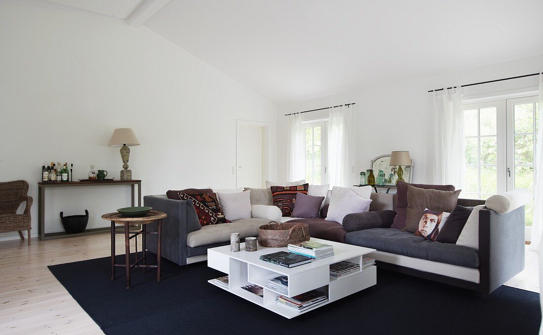 Moderner Weisser Couchtisch mit Öffnungen vor Ecksofa auf dunkelblauem Teppich in grossräumigem Wohnzimmer