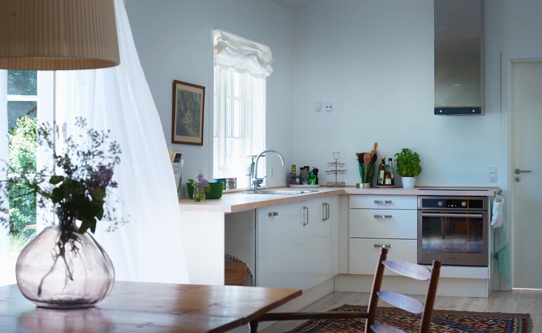 Moderne Landhaus-Küchenzeile Übereck, im Vordergrund Glasvase auf Holztisch