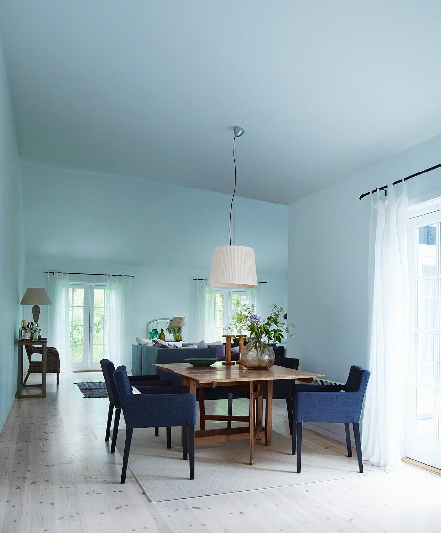 Gepolsterte Stühle mit blauem Stoffbezug um Holztisch in offenem Wohnraum mit minimalistischem Flair