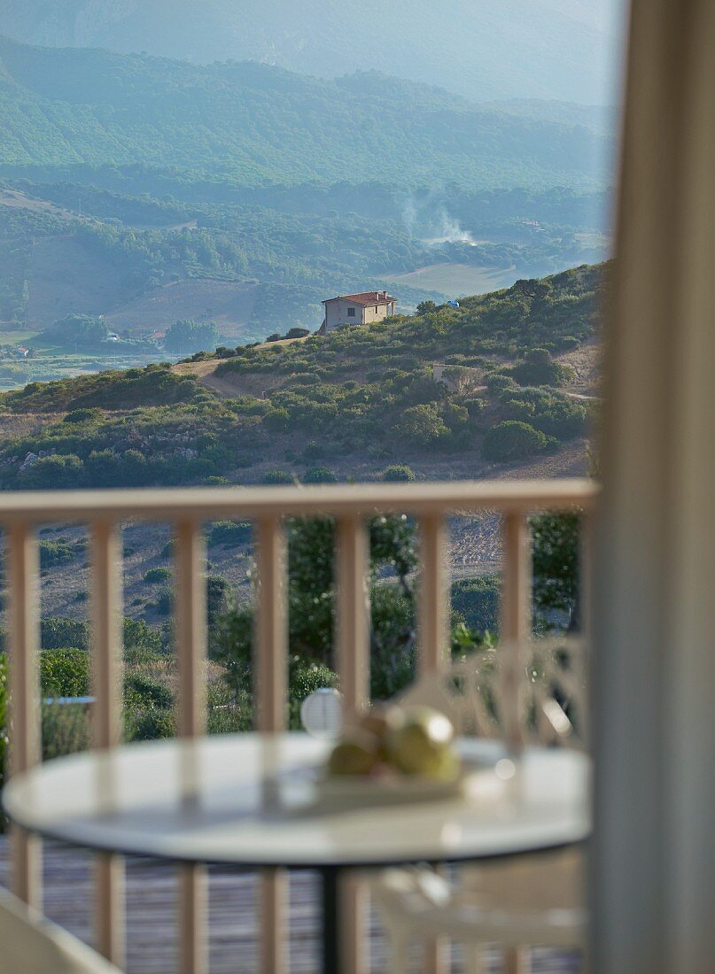 Blick durch Fenster über Balkon auf Berglandschaft und mediterranes, freistehendes Wohnhaus