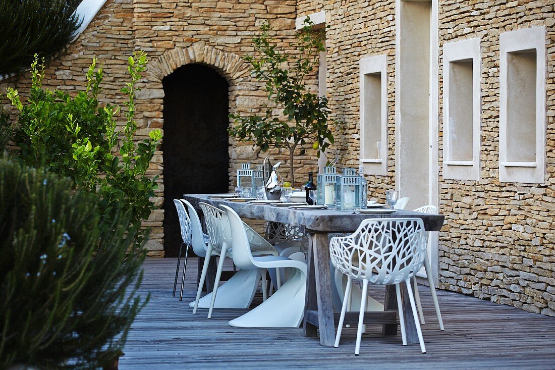 weiße Outdoor-Stühle um rustikalem Holztisch auf Terrasse vor mediterranem Natursteinhaus
