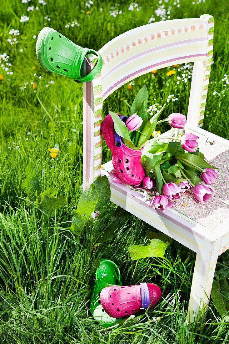 Tulips and garden clogs on child's chair in tall grass