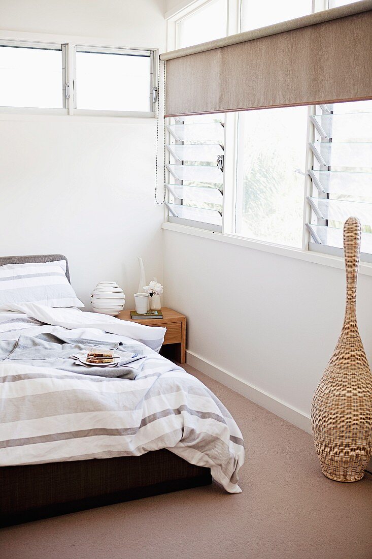 Bett mit gestreifter Bettwäsche in graubraunen Tönen in Schlafzimmerecke mit Fenster