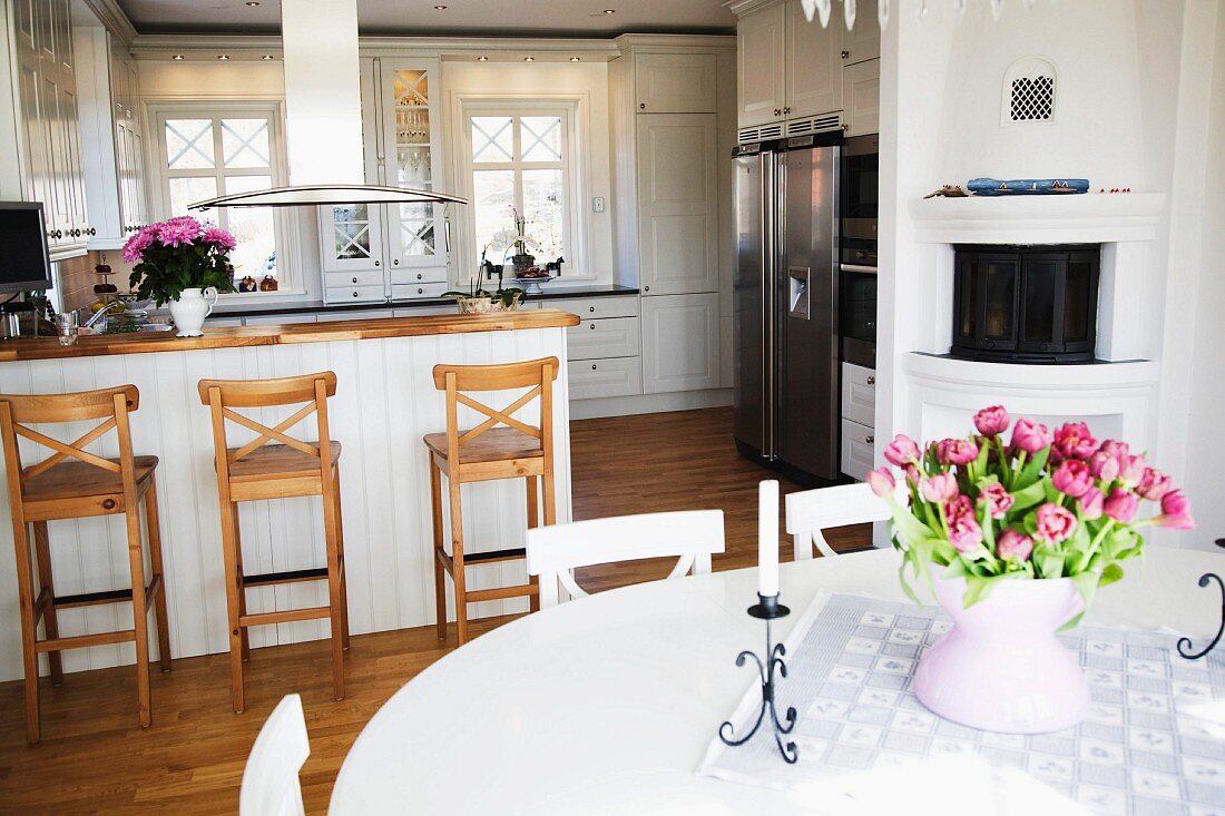 Tulpenstrausss auf weißem Esstisch, im Hintergrund Theke und Barhocker vor offener Landhausküche in Weiß