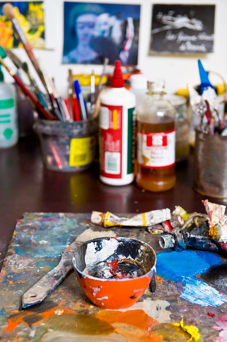 Schale mit Farbresten und Pinsel auf Arbeitstisch eines Malerateliers