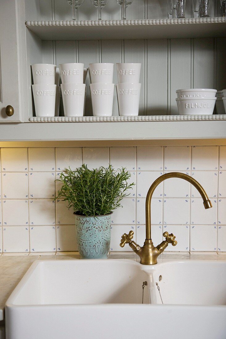Twin sink with vintage brass taps below crockery on pale grey wall-mounted shelves