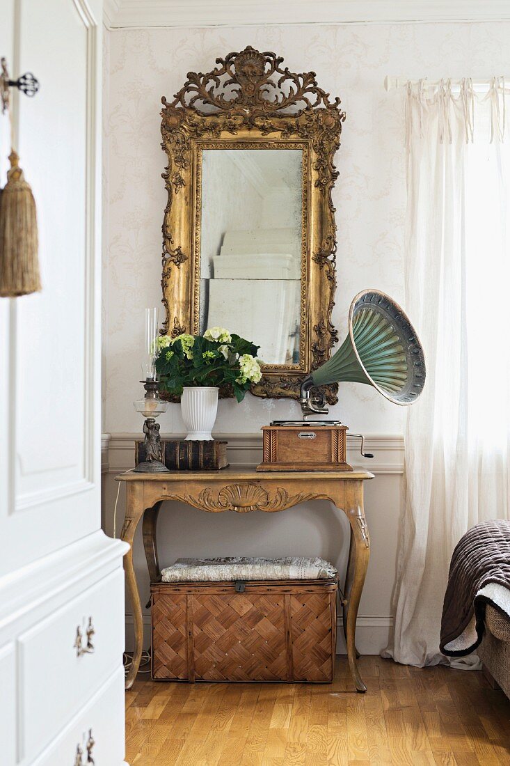Vintage gramophone on console table with curved legs below antique, gilt-framed mirror on wall