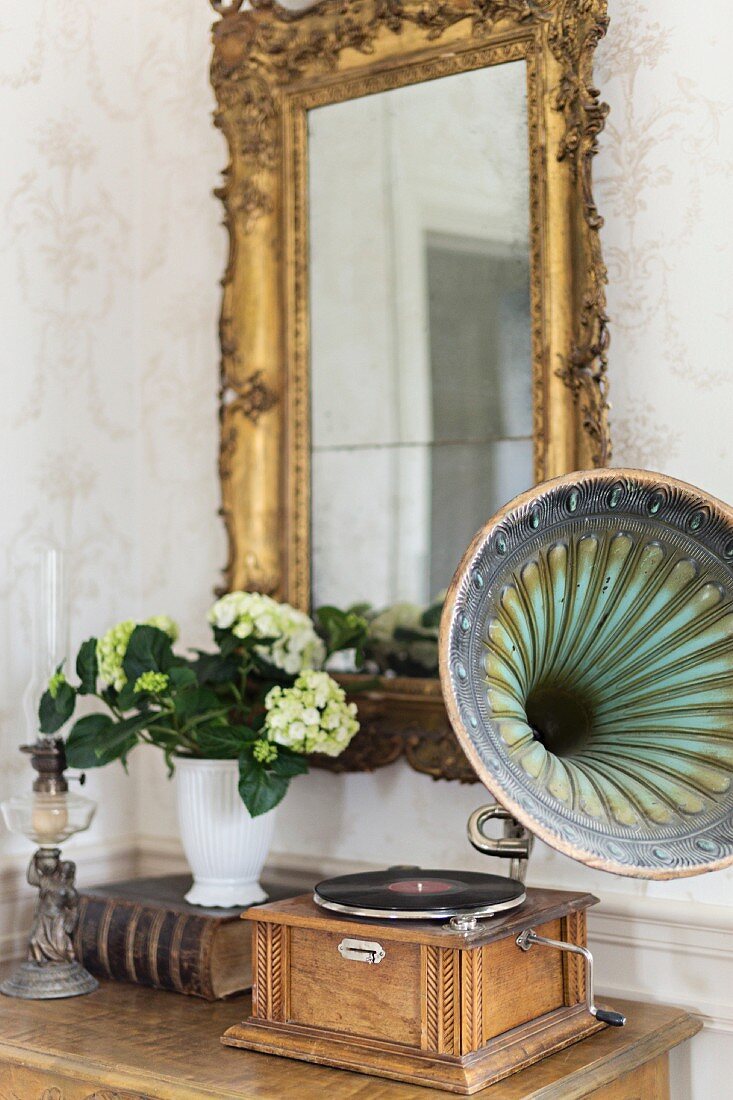 Vintage gramophone on console table below gilt-framed mirror on wall