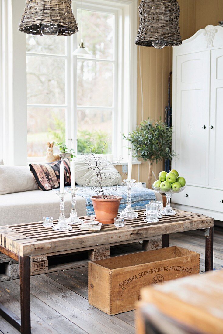 Rustic, DIY wooden coffee table and couch with pale cushions below window in rustic interior