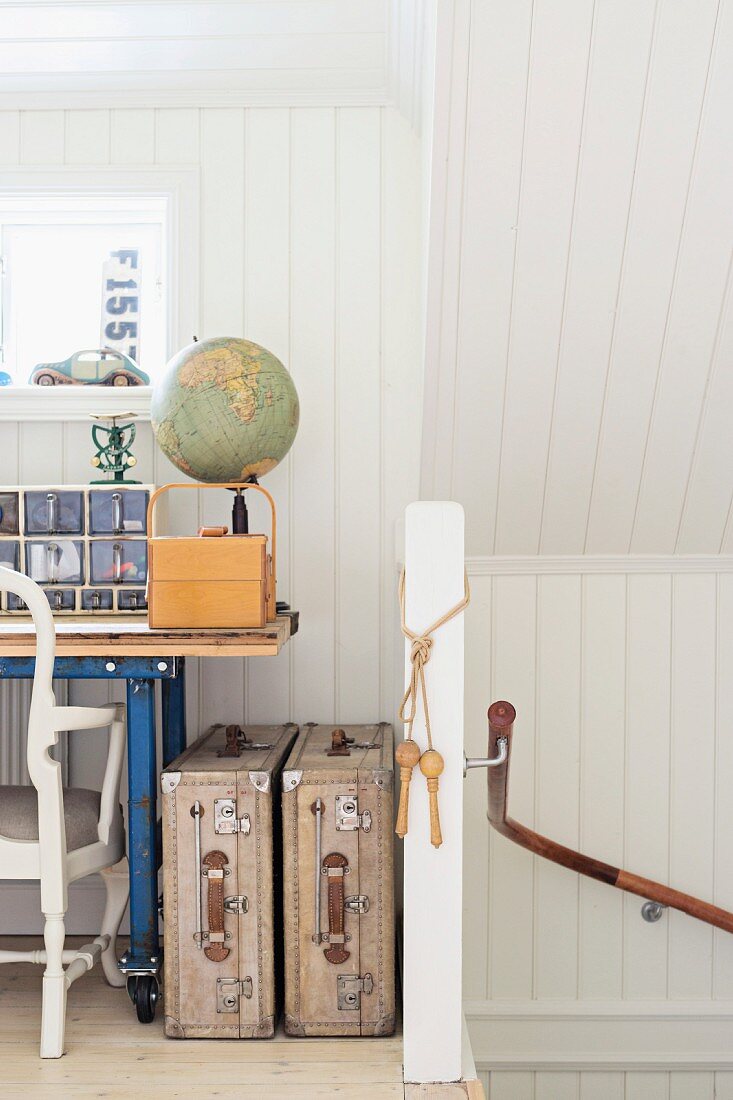 Offener Dachraum mit weisser Holzverkleidung, Ausschnitt eines Schreibtisches und Vintage Koffer neben Treppenhaus Wand