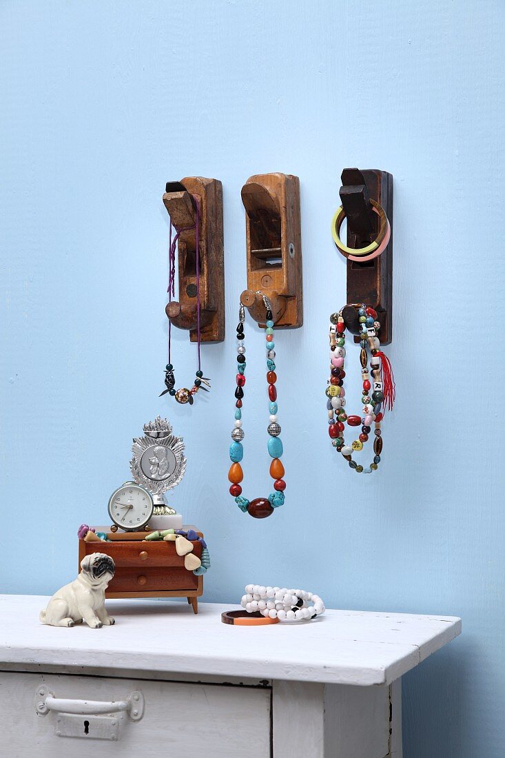 Alte Holzhobel als dekorative Haken für Halsketten; weiss lackierte Kommode mit Dekoobjekten vor blauer Wand