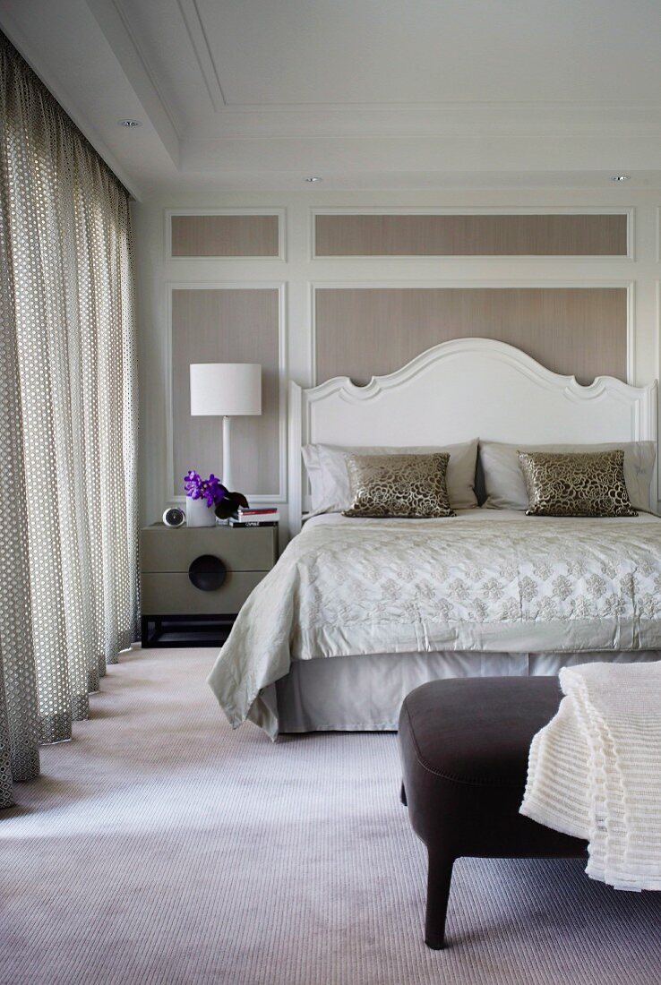 Elegantes Schlafzimmer, Doppelbett mit geschwungenem Holz Kopfteil in Weiß lackiert, vor Holzpaneelwand mit weißem Rahmen