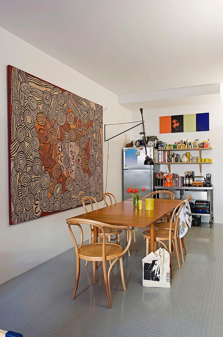Grossformatiges Aborigines-Kunstwerk hinter Esstisch mit Bugholzstühlen, bunt bestücktes Küchenregal im Hintergrund