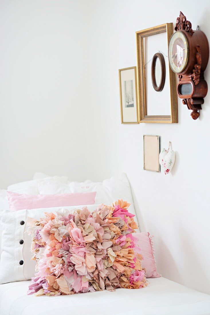 Scatter cushion with pink ruffles on couch below antique clock and various framed picture on wall