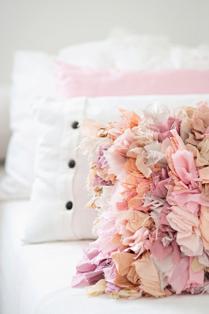 Scatter cushion with ruffles in shades of pink leaning against other cushions