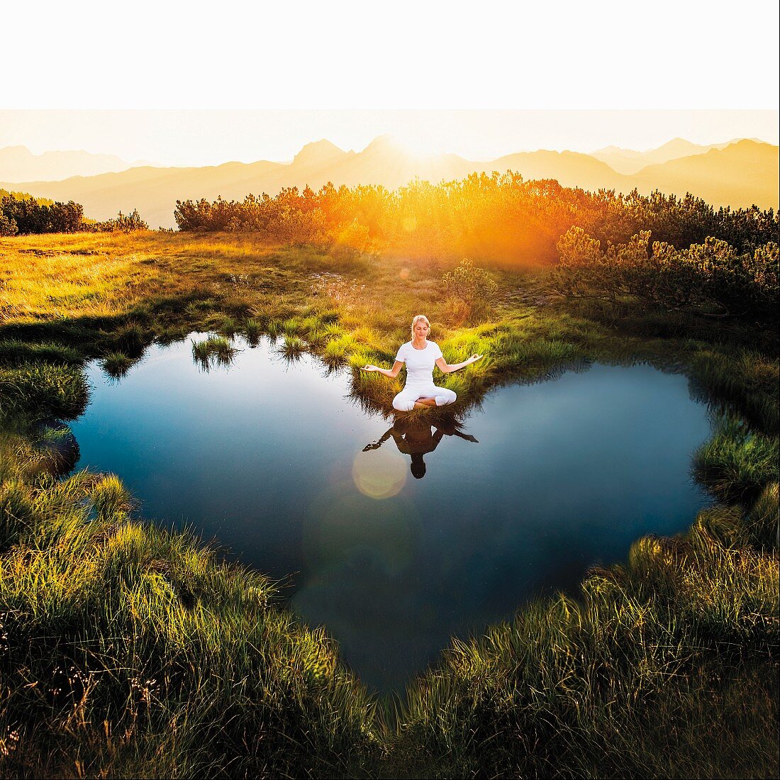 Woman meditating next to heart-shaped mountain pond