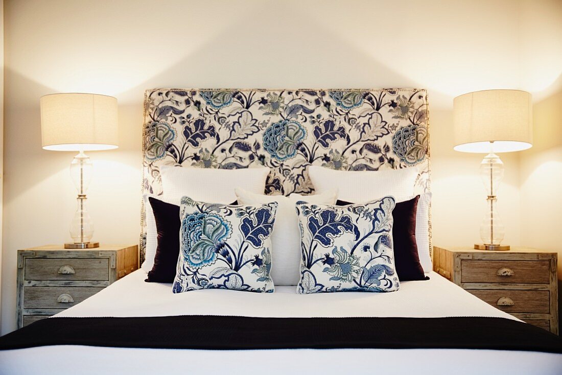 Stilvolles Schlafzimmer mit Doppelbett im Blumenmuster, Dekokissen und Nachtkästchen mit Lampen
